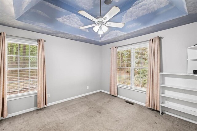 carpeted empty room featuring baseboards, a ceiling fan, a raised ceiling, and visible vents