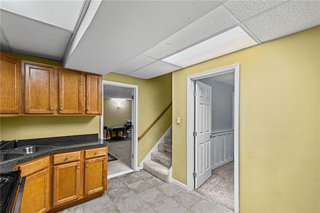 kitchen with brown cabinetry, range with gas stovetop, baseboards, a paneled ceiling, and a sink