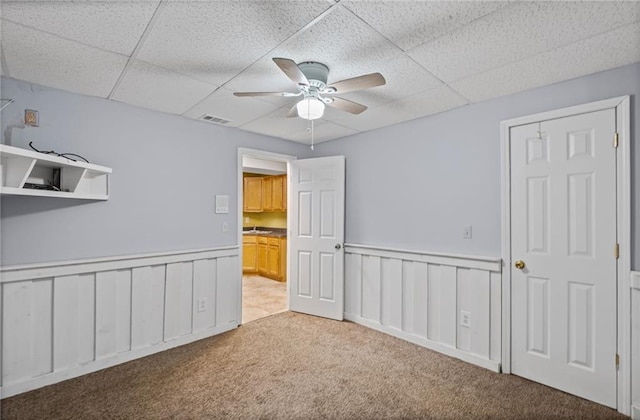 spare room with wainscoting, carpet floors, a paneled ceiling, a ceiling fan, and visible vents