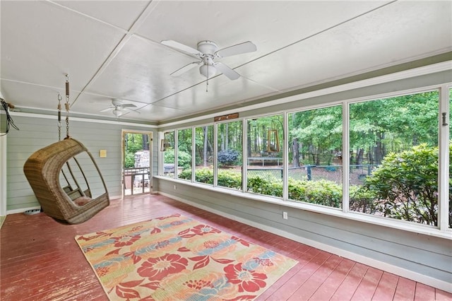 unfurnished sunroom with a ceiling fan, baseboards, wood walls, and hardwood / wood-style floors