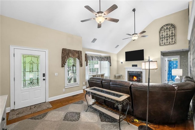 living area with ceiling fan, wood finished floors, baseboards, a warm lit fireplace, and lofted ceiling