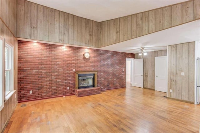 unfurnished living room with light wood-type flooring, wood walls, ceiling fan, brick wall, and a fireplace