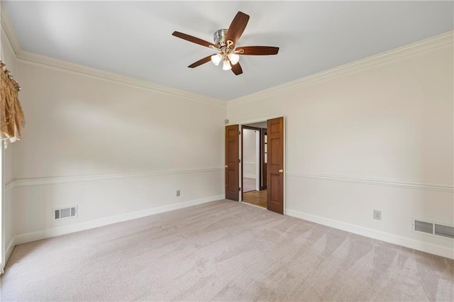 spare room featuring ceiling fan, visible vents, baseboards, ornamental molding, and light carpet