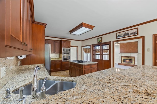 kitchen with a sink, ornamental molding, stainless steel appliances, and a glass covered fireplace