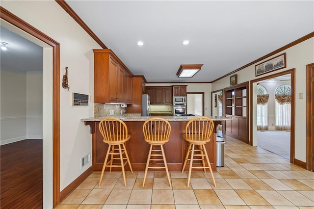 kitchen with ornamental molding, decorative backsplash, a peninsula, baseboards, and appliances with stainless steel finishes