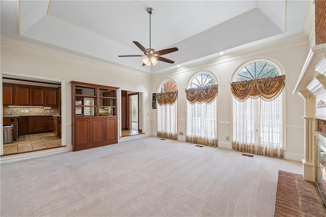 unfurnished living room featuring a ceiling fan, a brick fireplace, a high ceiling, and a tray ceiling