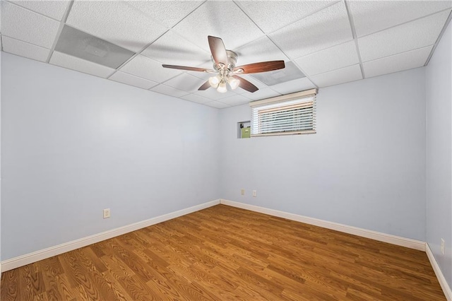 empty room with baseboards, ceiling fan, wood finished floors, and a paneled ceiling