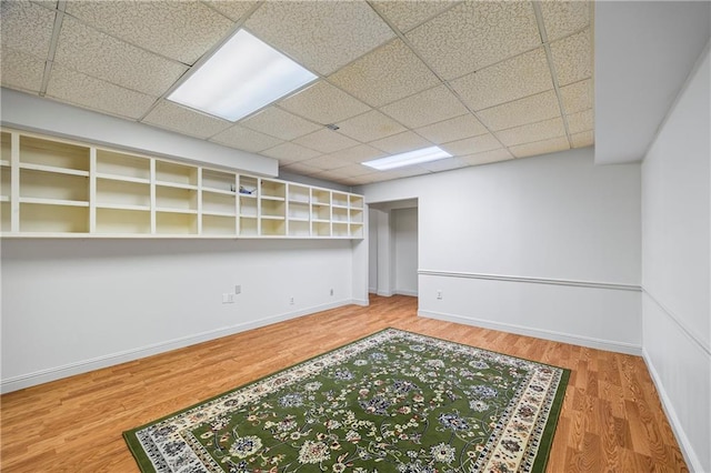 finished below grade area featuring baseboards, a drop ceiling, and wood finished floors