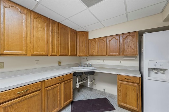 kitchen with a paneled ceiling, brown cabinets, a sink, and white refrigerator with ice dispenser