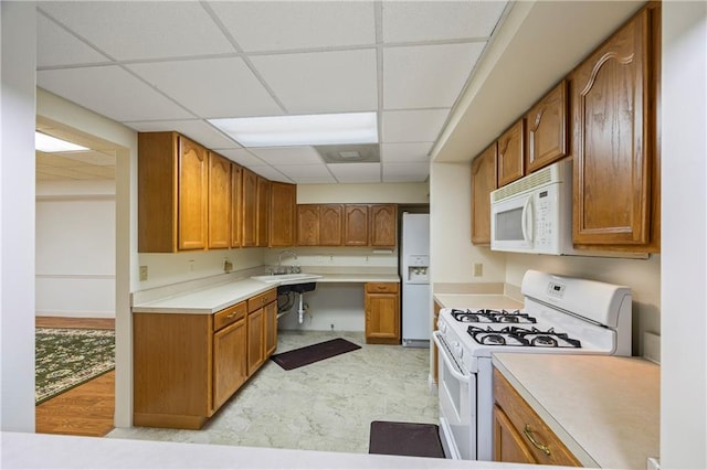 kitchen featuring brown cabinetry, white appliances, a drop ceiling, light countertops, and a sink
