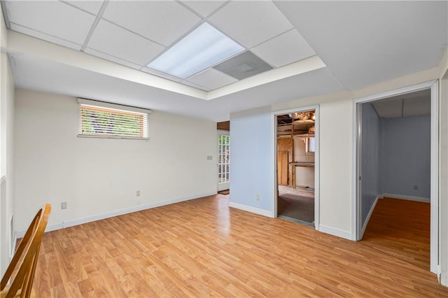 empty room with baseboards, plenty of natural light, light wood finished floors, and a paneled ceiling