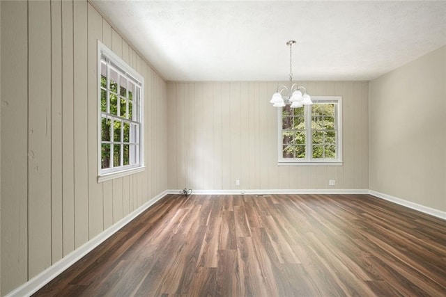 unfurnished room featuring wood finished floors, a chandelier, baseboards, and wood walls