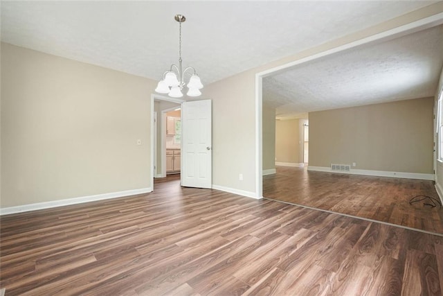 unfurnished room with wood finished floors, a chandelier, and baseboards