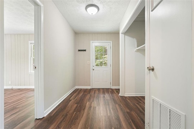 entryway with dark wood finished floors, a textured ceiling, baseboards, and wooden walls
