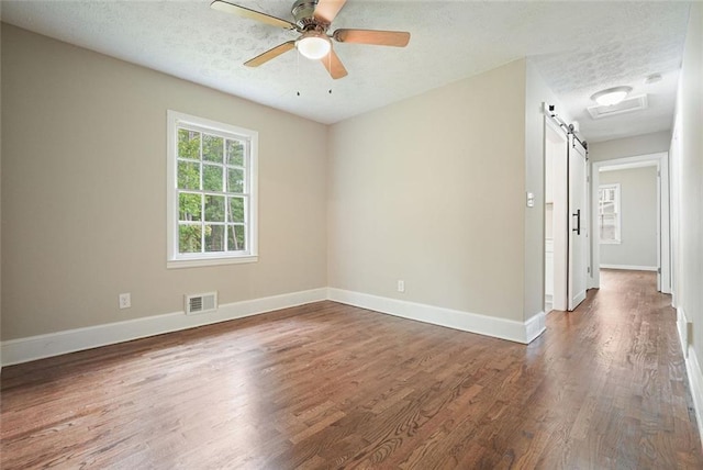 empty room with a textured ceiling, wood finished floors, a ceiling fan, baseboards, and a barn door