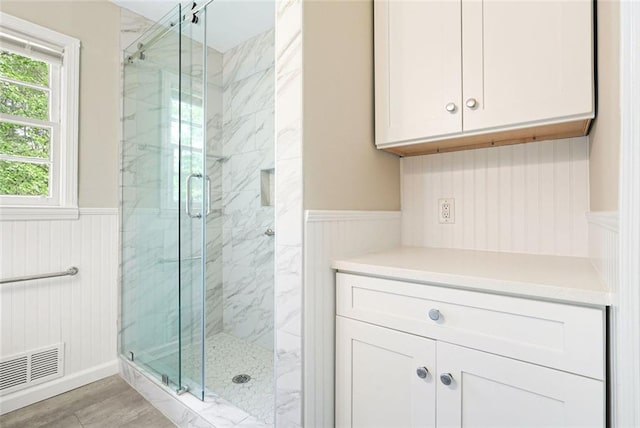 full bath featuring wainscoting, a marble finish shower, and wood finished floors