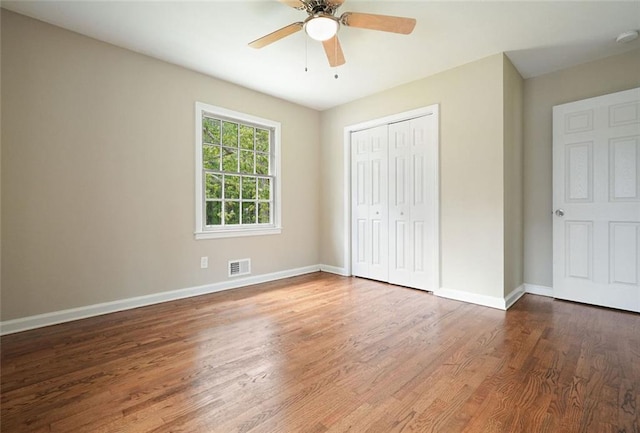 unfurnished bedroom featuring wood finished floors, a closet, baseboards, and a ceiling fan