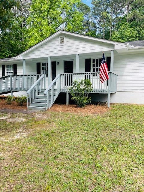 view of front of house featuring a porch, a front lawn, and view of wooded area