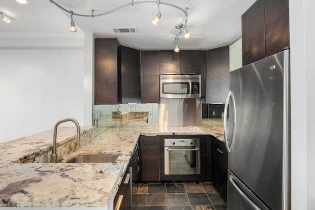 kitchen with appliances with stainless steel finishes, kitchen peninsula, light stone countertops, and dark brown cabinetry