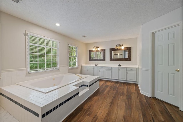 bathroom with a textured ceiling, vanity, hardwood / wood-style flooring, and a relaxing tiled tub