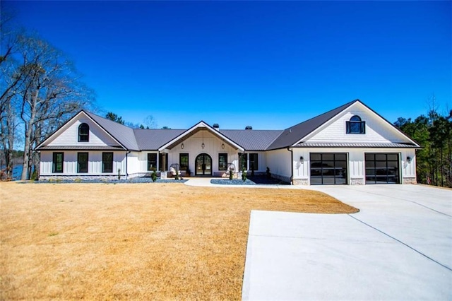 modern farmhouse style home featuring concrete driveway, an attached garage, a front yard, a standing seam roof, and metal roof