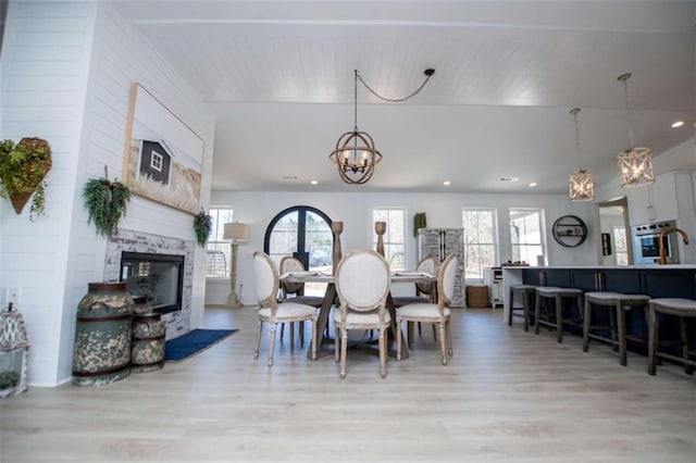 dining space featuring light wood-style floors, a glass covered fireplace, recessed lighting, and an inviting chandelier