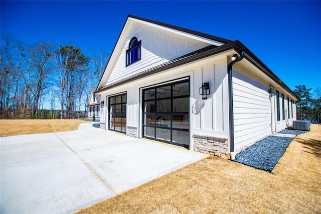 view of property exterior featuring a garage, board and batten siding, a patio, stone siding, and central AC