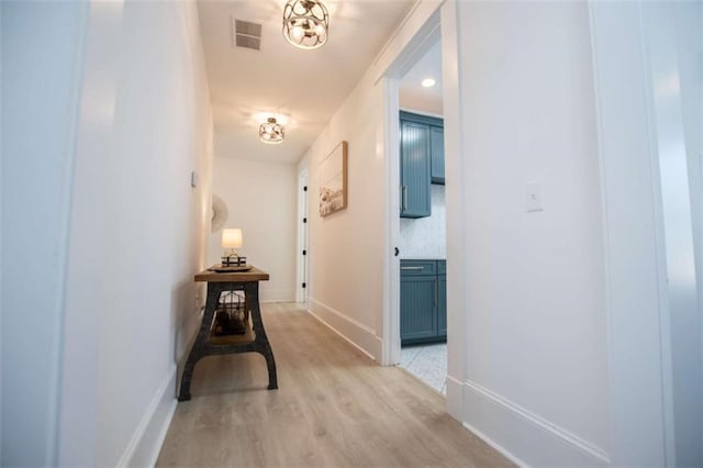 corridor featuring baseboards, visible vents, and light wood finished floors