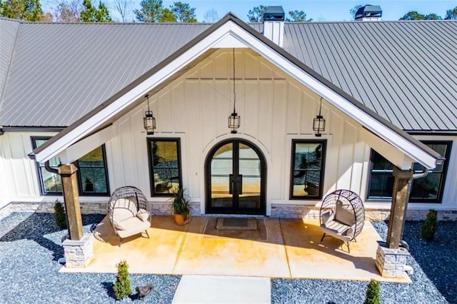 entrance to property with french doors, a patio, board and batten siding, metal roof, and stone siding