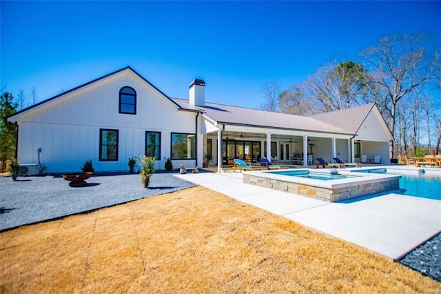 rear view of property featuring an outdoor pool, a patio, a chimney, metal roof, and an in ground hot tub