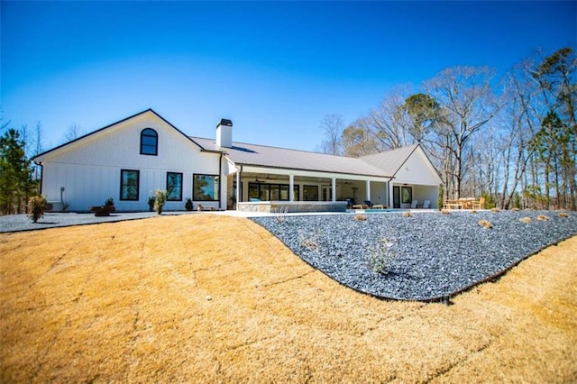 back of house featuring a yard, metal roof, and a chimney