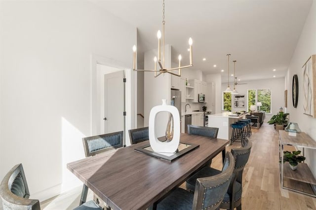 dining area with an inviting chandelier, sink, and light hardwood / wood-style flooring