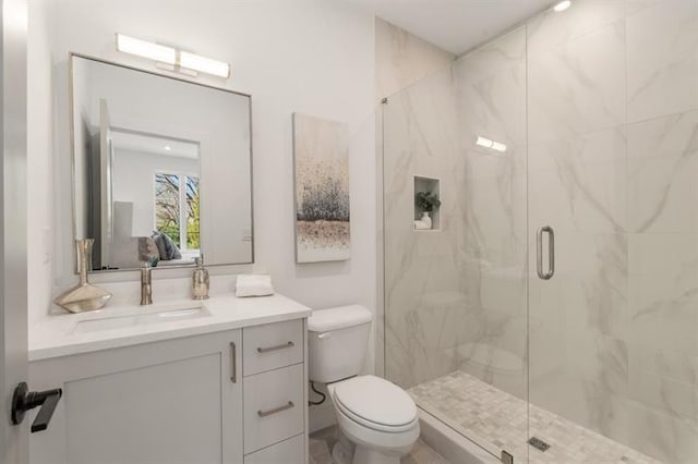 bathroom featuring a shower with door, vanity, and toilet