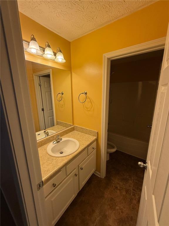 bathroom featuring tile patterned flooring, vanity, a textured ceiling, and toilet