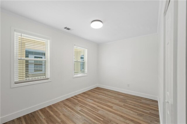 spare room with ornamental molding, visible vents, baseboards, and wood finished floors