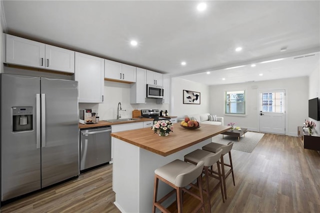 kitchen featuring stainless steel appliances, butcher block counters, wood finished floors, a sink, and a kitchen breakfast bar