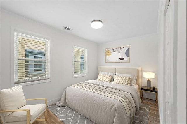 bedroom featuring ornamental molding, visible vents, baseboards, and wood finished floors