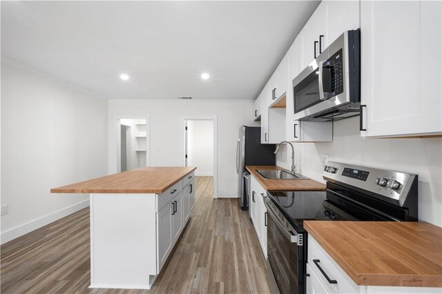 kitchen with a kitchen island, wood counters, appliances with stainless steel finishes, white cabinetry, and a sink