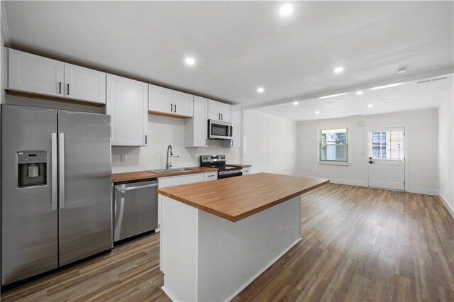 kitchen with butcher block countertops, wood finished floors, a center island, stainless steel appliances, and a sink