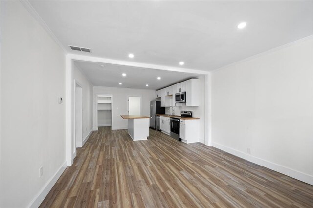 kitchen with butcher block countertops, wood finished floors, stainless steel appliances, white cabinetry, and a sink