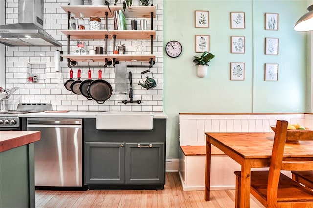 kitchen with backsplash, wall chimney range hood, sink, light hardwood / wood-style floors, and stainless steel appliances