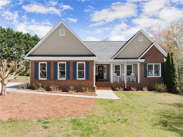view of front of property with a front lawn, a porch, brick siding, and roof with shingles