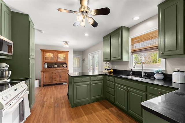 kitchen with green cabinets, white range with electric cooktop, a sink, dark countertops, and a peninsula