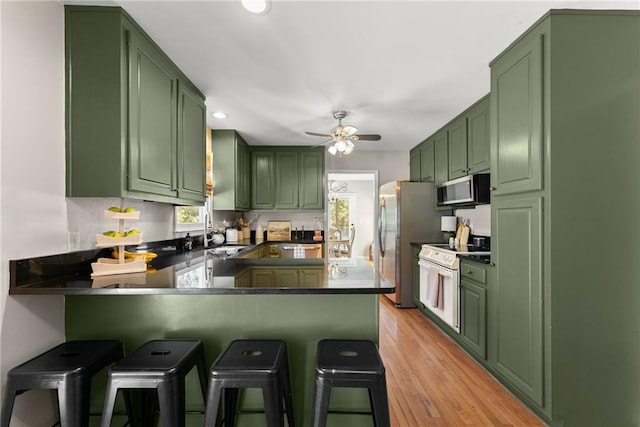 kitchen with green cabinetry, a sink, stainless steel appliances, and dark countertops