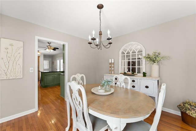 dining space with baseboards, ceiling fan with notable chandelier, and hardwood / wood-style flooring
