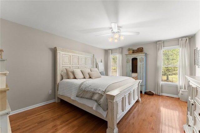 bedroom featuring light wood-style flooring, baseboards, multiple windows, and ceiling fan