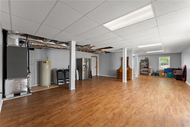 basement featuring a paneled ceiling, water heater, stainless steel fridge with ice dispenser, and wood finished floors