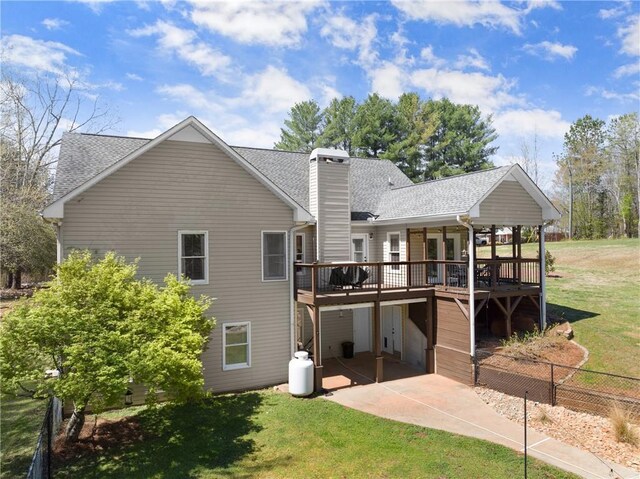 rear view of house with a chimney, a patio, a deck, and a lawn