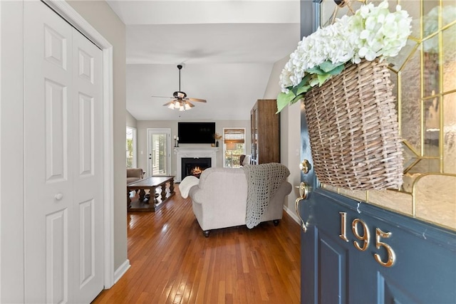 entrance foyer with a lit fireplace, wood-type flooring, lofted ceiling, baseboards, and ceiling fan