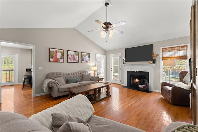 living area with a fireplace with flush hearth, baseboards, ceiling fan, lofted ceiling, and light wood-type flooring